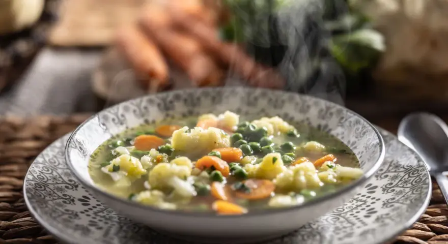 Zuppa fumante con cavolfiore, piselli e carote, arricchita da un tocco di panna da cucina per una cremosità avvolgente.