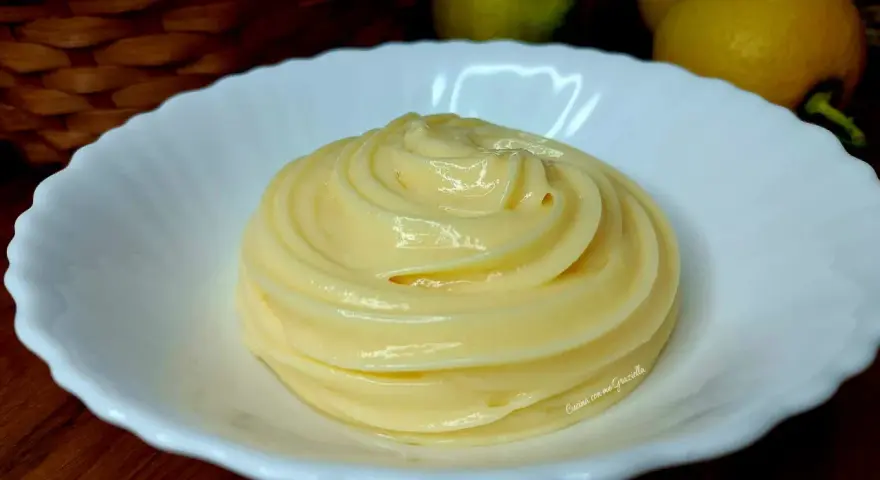 Una spirale di soffice crema al limone in una ciotola bianca, con limoni e uova sullo sfondo.