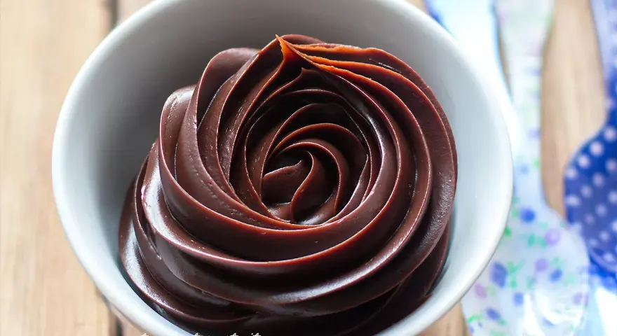 Una ciotola bianca piena di lucida ganache al cioccolato, disposta a spirale.