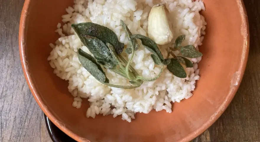 Riso in cagnone, profumato con aglio e salvia croccante, servito in una ciotola di terracotta.