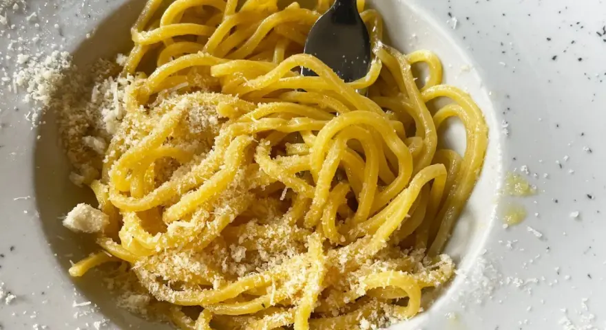 Un piatto di pasta in bianco, spaghetti conditi con formaggio grattugiato e un filo d'olio, pronti per essere gustati.