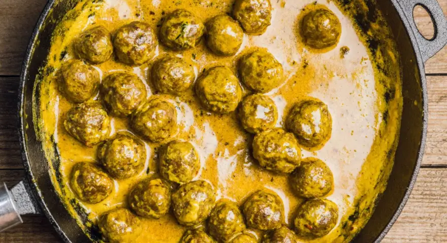 Polpette in bianco cremose in padella, dorate e succulente, immerse in una salsa gialla e invitante.
