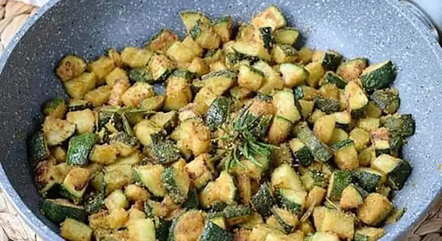 Zucchine gratinate in padella, dorate e saporite, con un rametto di rosmarino fresco.