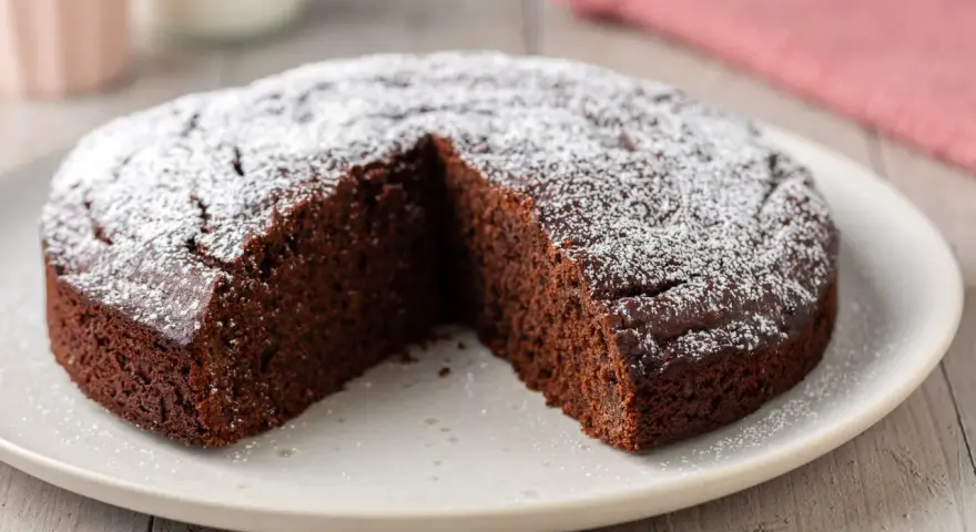 Una fetta è stata tolta da questa torta al cioccolato morbida, cosparsa di zucchero a velo.