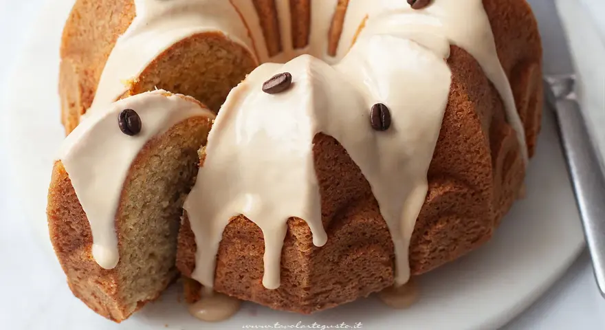 Deliziosa torta al caffè con glassa chiara e chicchi di caffè come decorazione. Una fetta è stata tagliata, mostrando la morbidezza dell'interno.