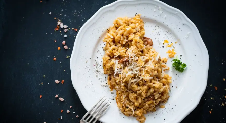 Un piatto di risotto funghi e salsiccia, guarnito con parmigiano grattugiato e prezzemolo, pronto per essere gustato.