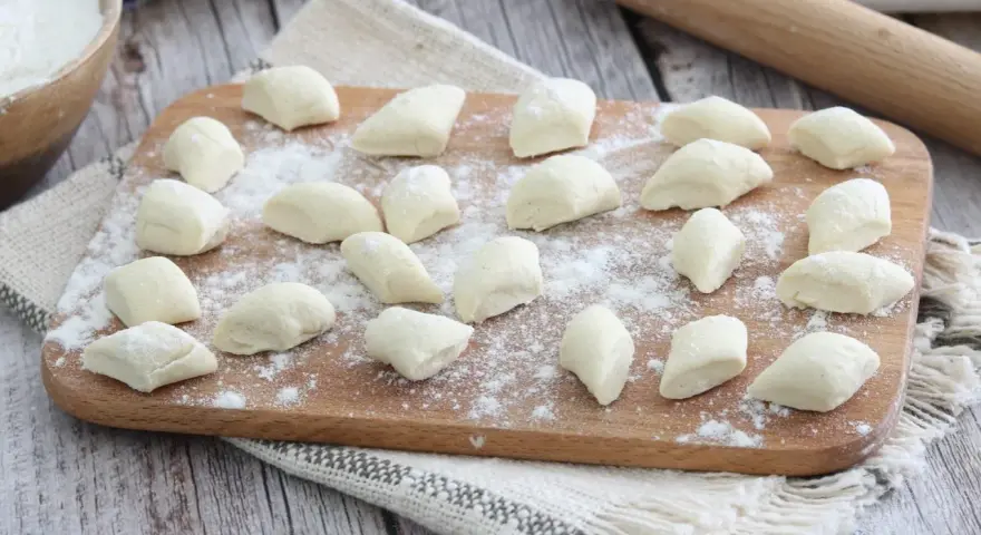 Gnocchi di ricotta freschi, pronti per essere cotti, spolverati di farina su un tagliere di legno.