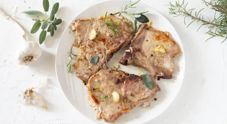 Tre succulente braciole di maiale cotte alla perfezione, guarnite con aglio, rosmarino e salvia.