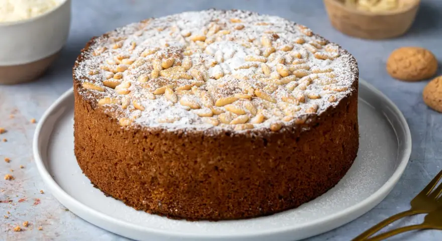 Torta soffice con farina di mandorle, ricoperta di pinoli e zucchero a velo. Perfetta per una pausa golosa.