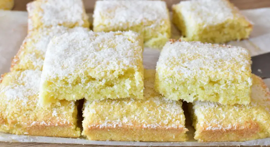 Fette di torta al cocco, soffici e dorate, cosparse di scaglie bianche. Un dolce profumato e invitante.