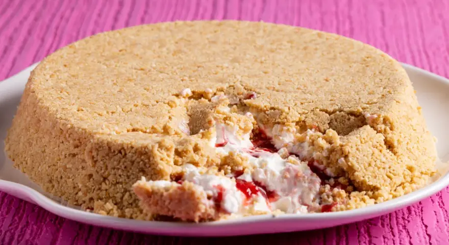 Cheesecake con yogurt greco e marmellata di fragole, con una crosta friabile di biscotti. Un morso goloso rivela il ripieno cremoso.