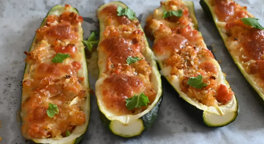 Zucchine tonde ripiene al forno, dorate e filanti, guarnite con foglie di menta fresca.