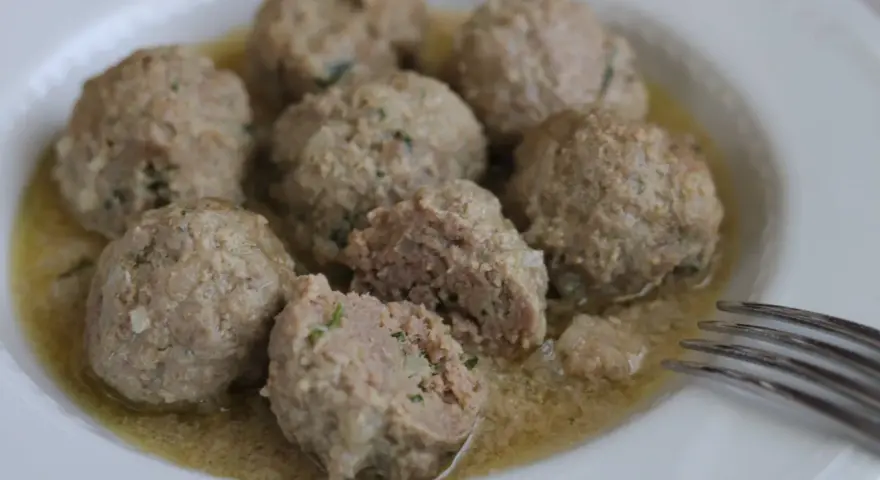 Polpette in umido, morbide e succulente, servite in un piatto bianco con un sughetto invitante.