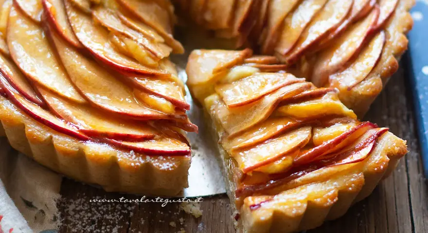 Una fetta di crostata di mele lucida e dorata, con le mele disposte a spirale su una base friabile.