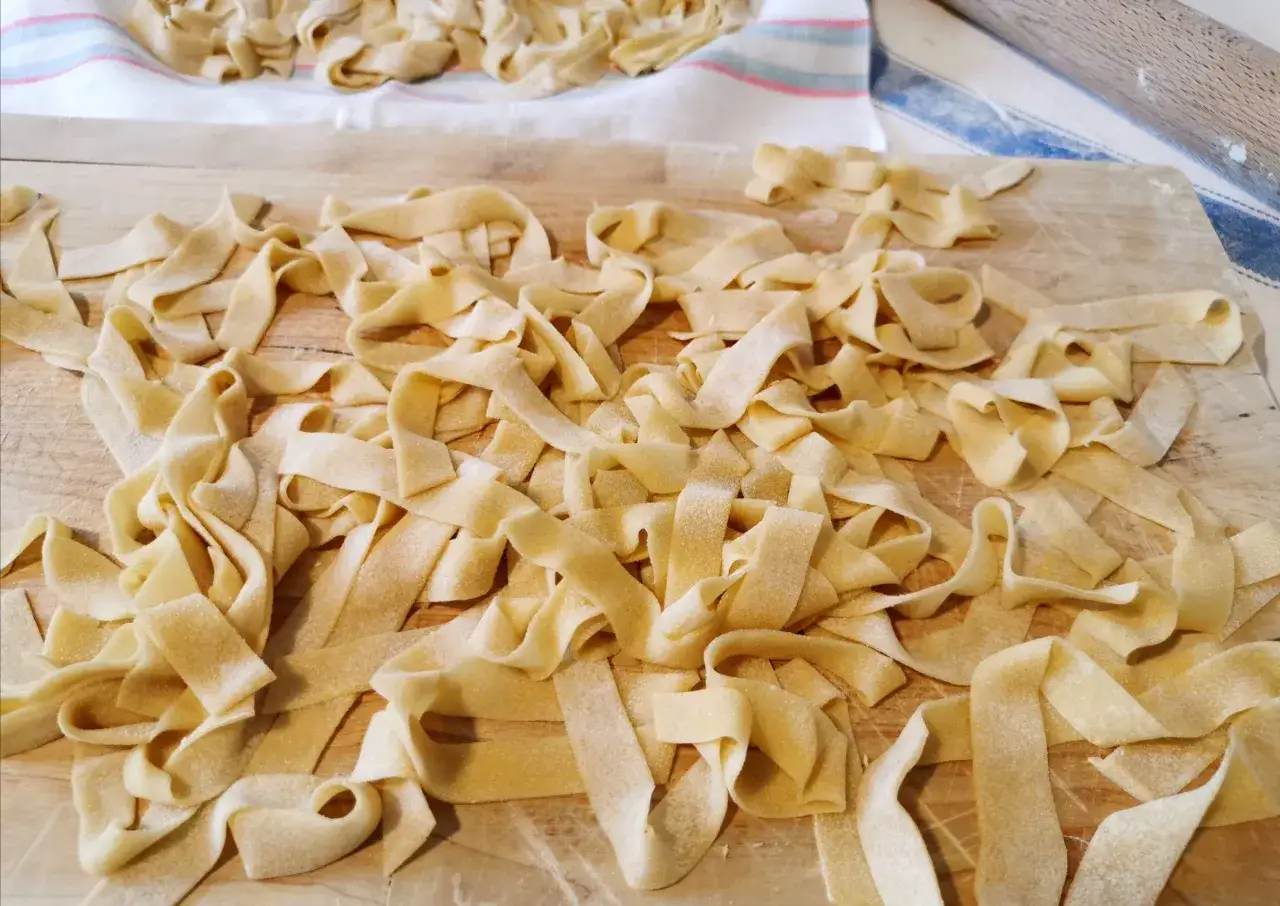 Tagliatelle fatte in casa, pronte per essere cucinate, sparse su un tagliere di legno e un canovaccio a righe.