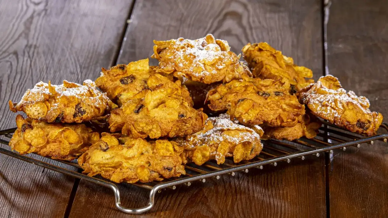 Biscotti croccanti, simili a rose del deserto, ricoperti di zucchero a velo su una griglia metallica.