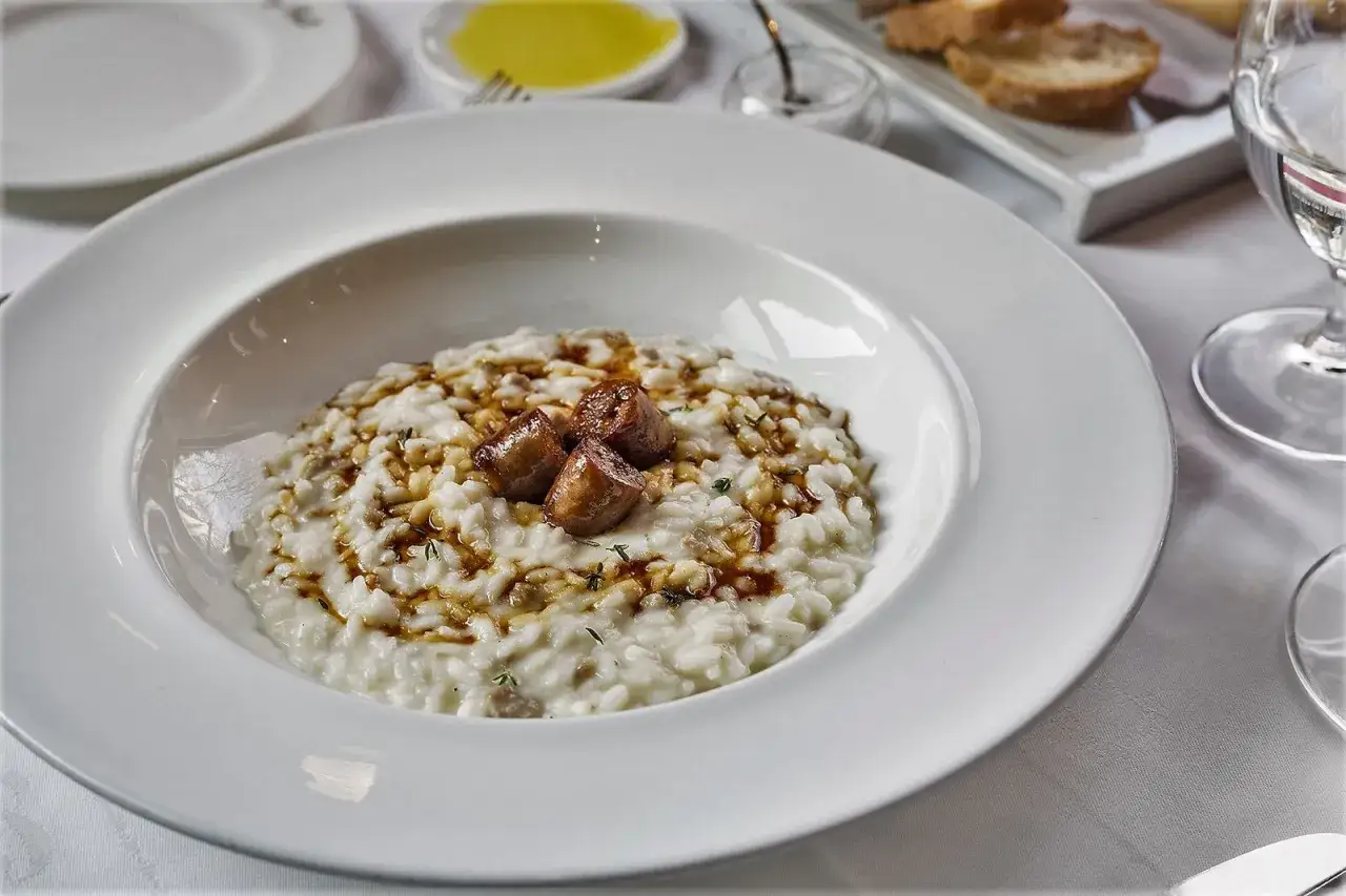 Un cremoso risotto alla monzese, guarnito con salsiccia e un filo d'olio, pronto per essere gustato.