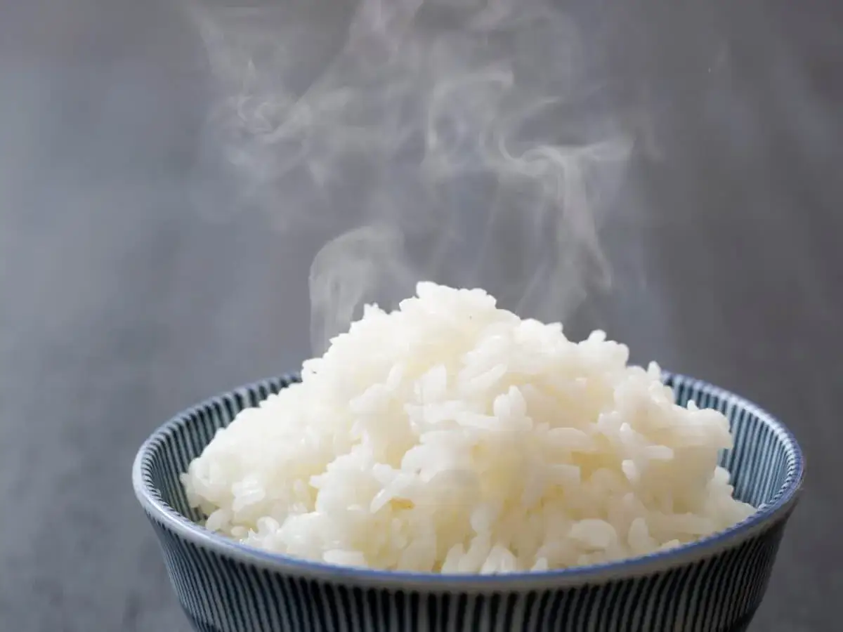 Una ciotola di riso in bianco fumante, con vapore che sale dolcemente. Un piatto semplice e confortante.