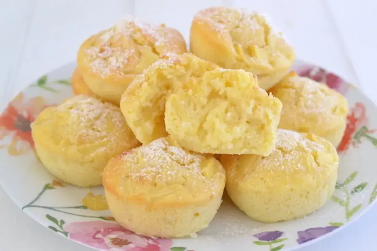 Un piatto di muffin alle mele soffici, spolverati di zucchero a velo. Uno &egrave; tagliato a met&agrave;, mostrando la morbida mollica e i pezzetti di mela.