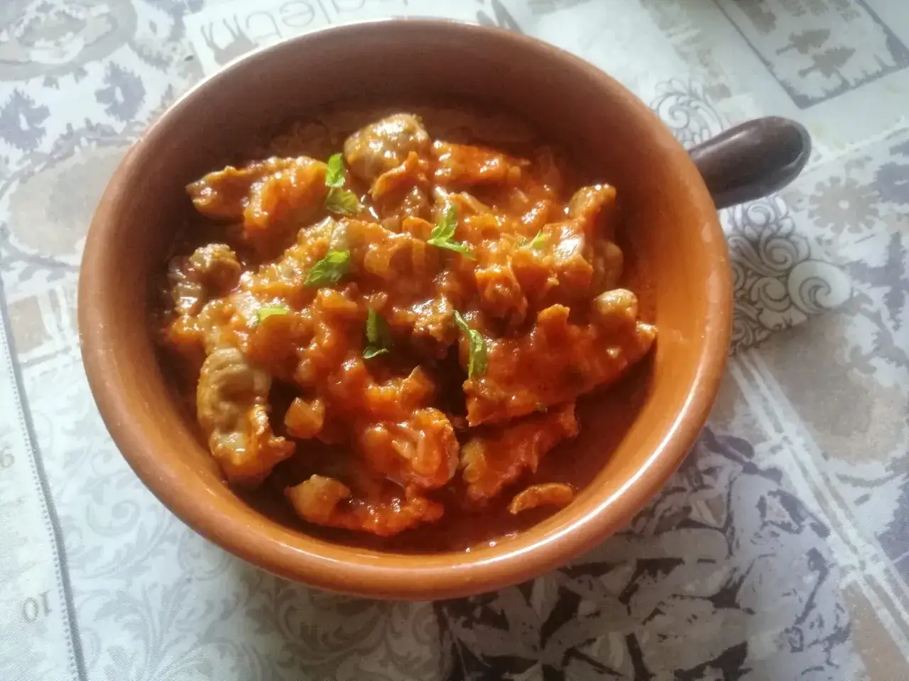 Un saporito piatto di durelli di pollo in umido, guarnito con foglie di menta fresca, servito in una ciotola di terracotta.