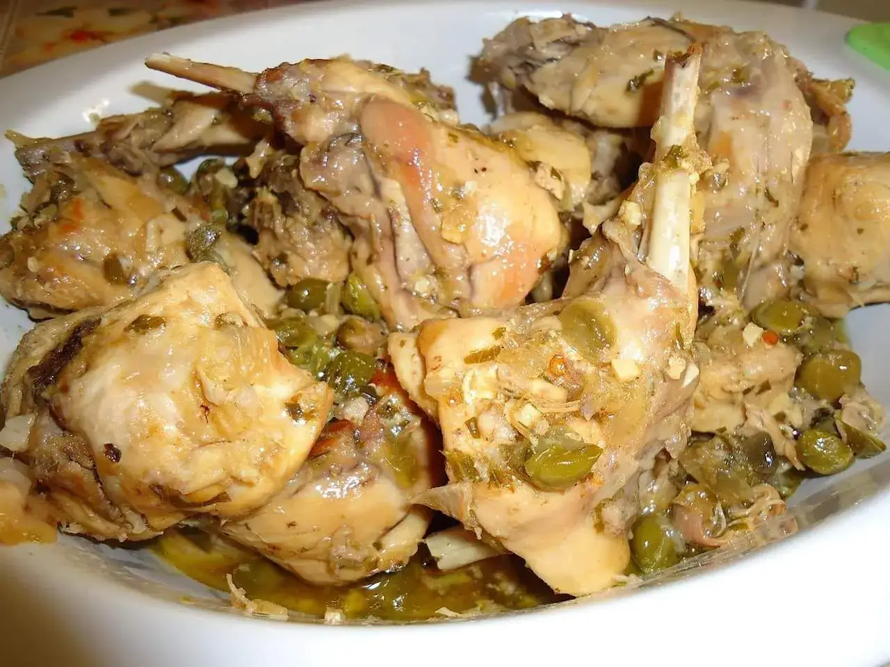 Un saporito coniglio alla cacciatora in bianco, con olive verdi e erbe aromatiche, servito in un piatto bianco.