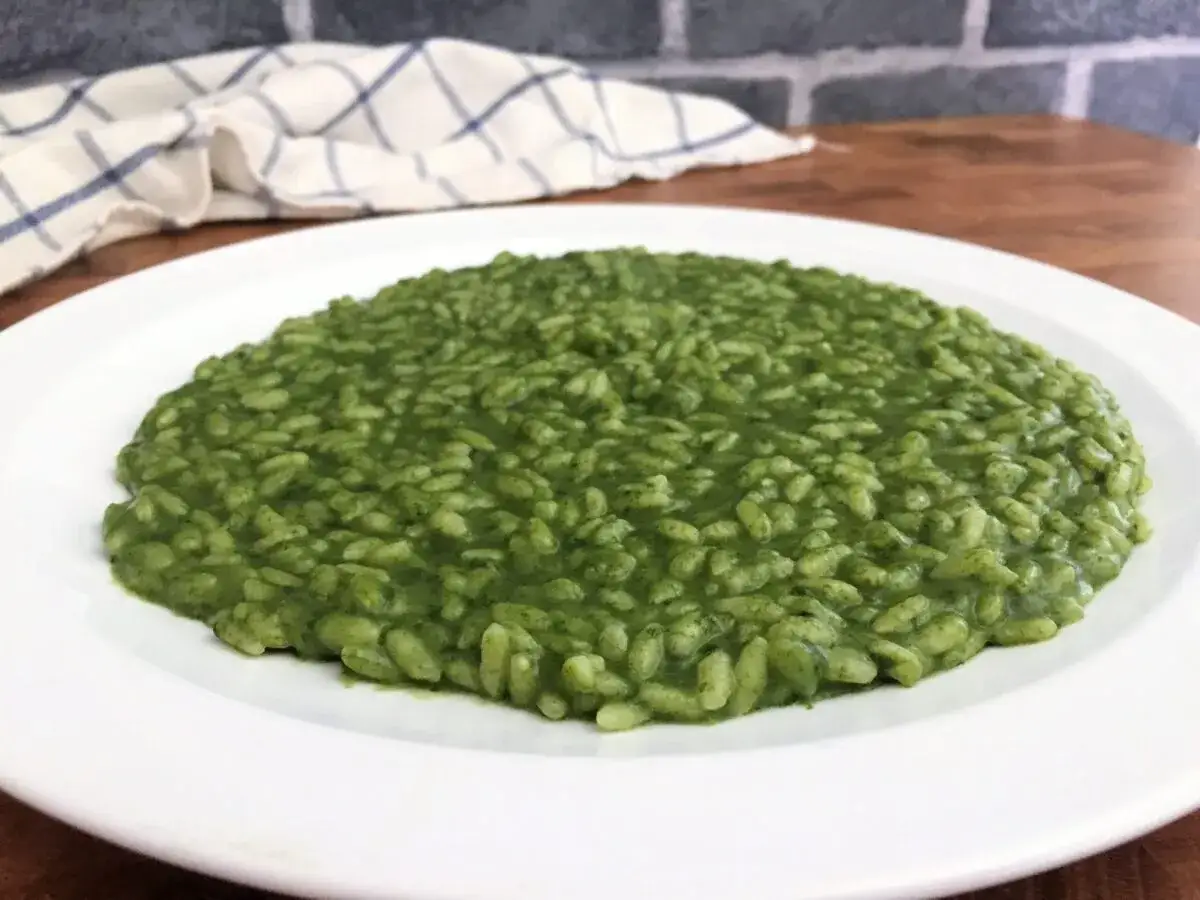 Un cremoso risotto con spinaci, servito su un piatto bianco. Un piatto invitante e colorato.