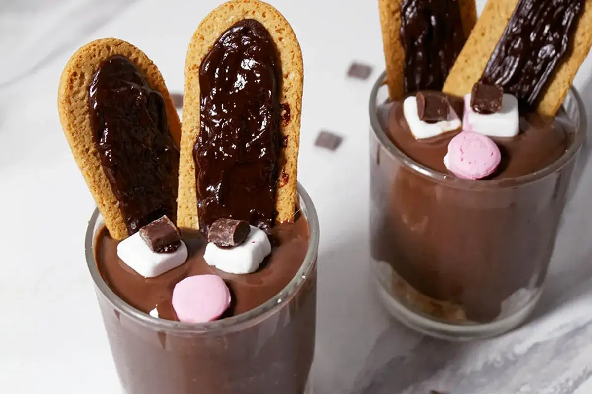Due bicchieri di cremoso budino al cioccolato decorati come coniglietti, con orecchie di biscotto e marshmallow.