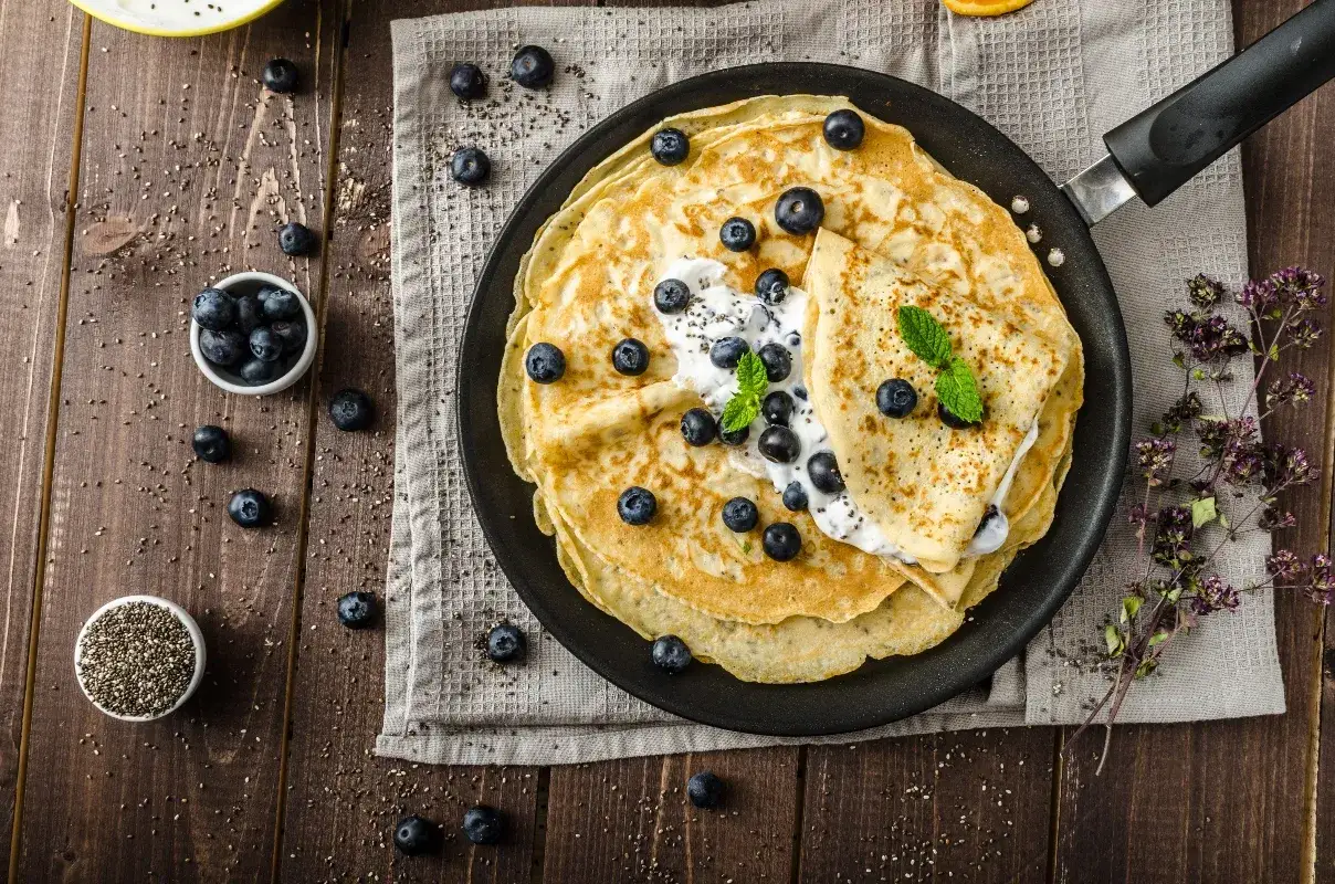 Deliziose crepes senza glutine, guarnite con yogurt, mirtilli freschi e menta, pronte per essere gustate.