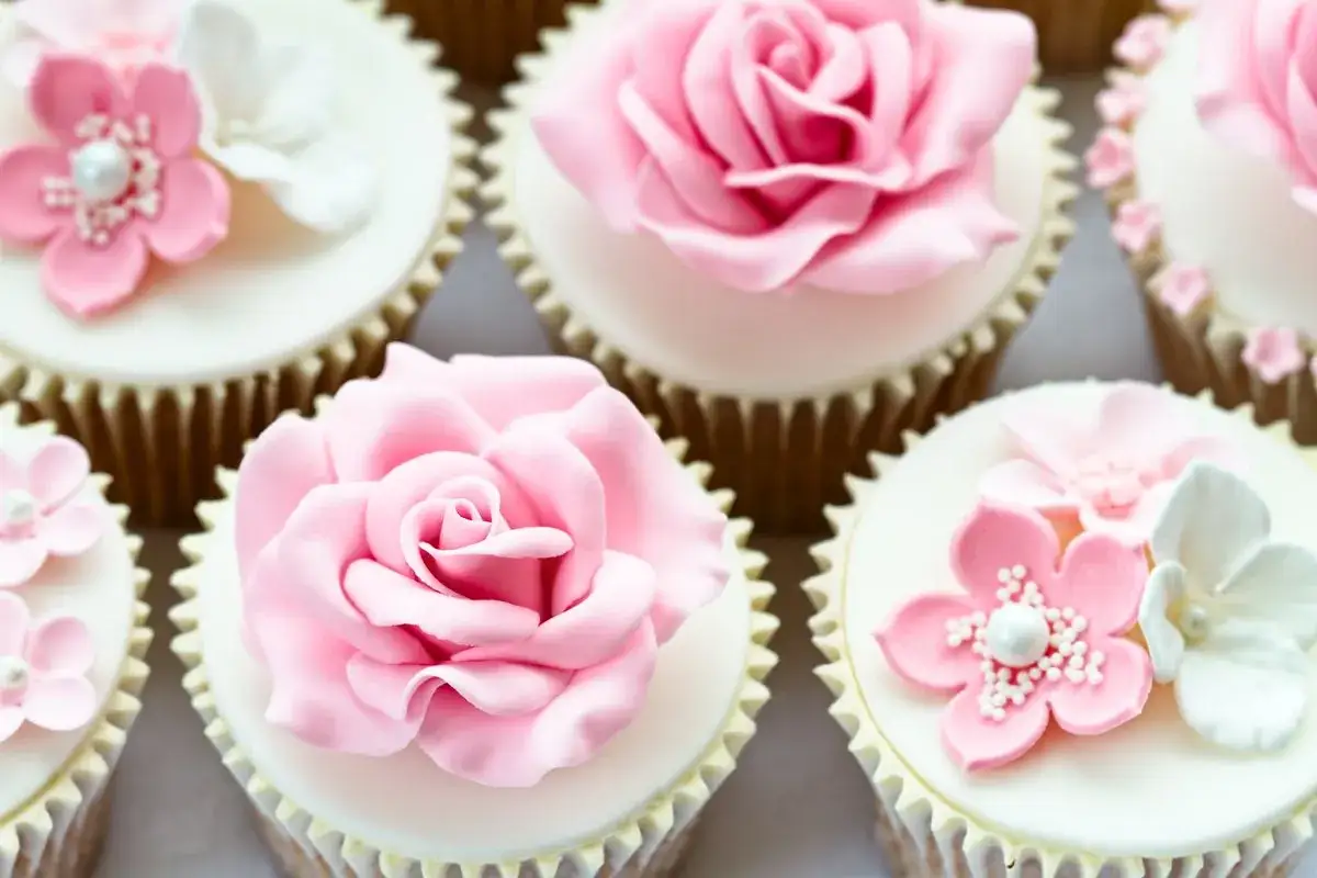 Delicati cupcake decorati con rose e fiori in pasta di zucchero rosa e bianchi, perfetti per un'occasione speciale.