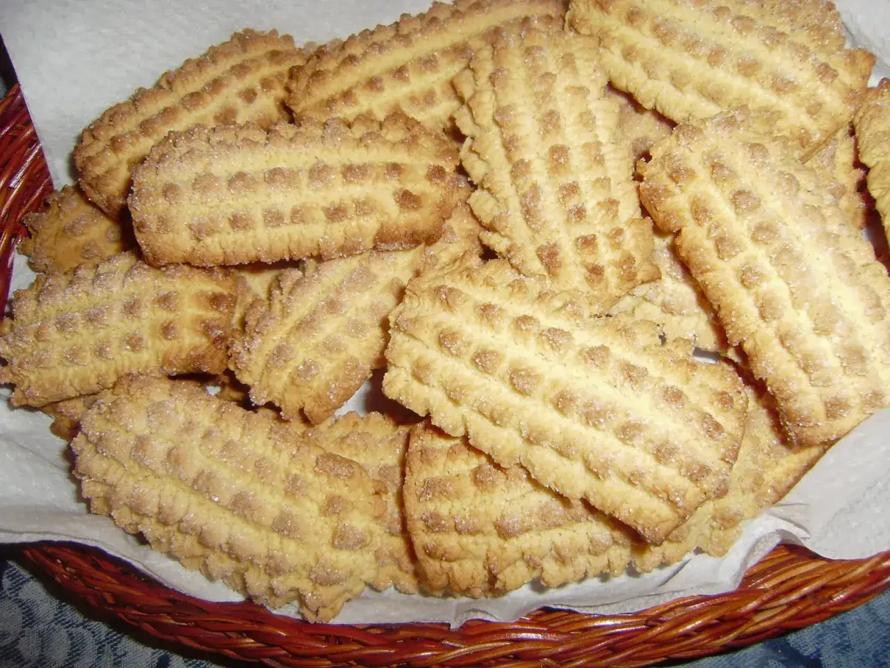 Un cesto pieno di biscotti da inzuppo dorati, con una trama a quadretti e un bordo seghettato, perfetti per la colazione.