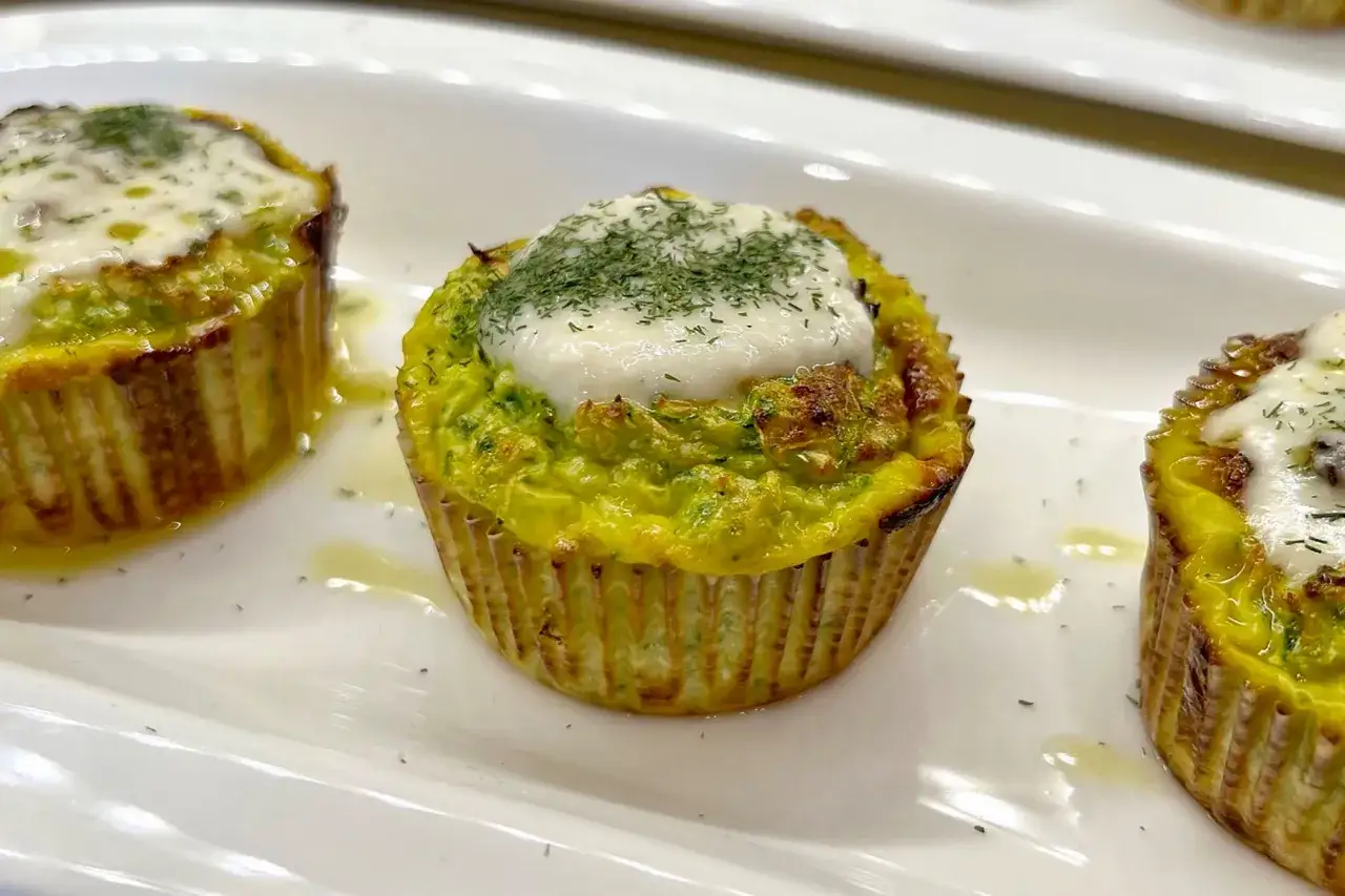 Tre flan di zucchine dorati, guarniti con formaggio fuso e erbe aromatiche, serviti su un piatto bianco.