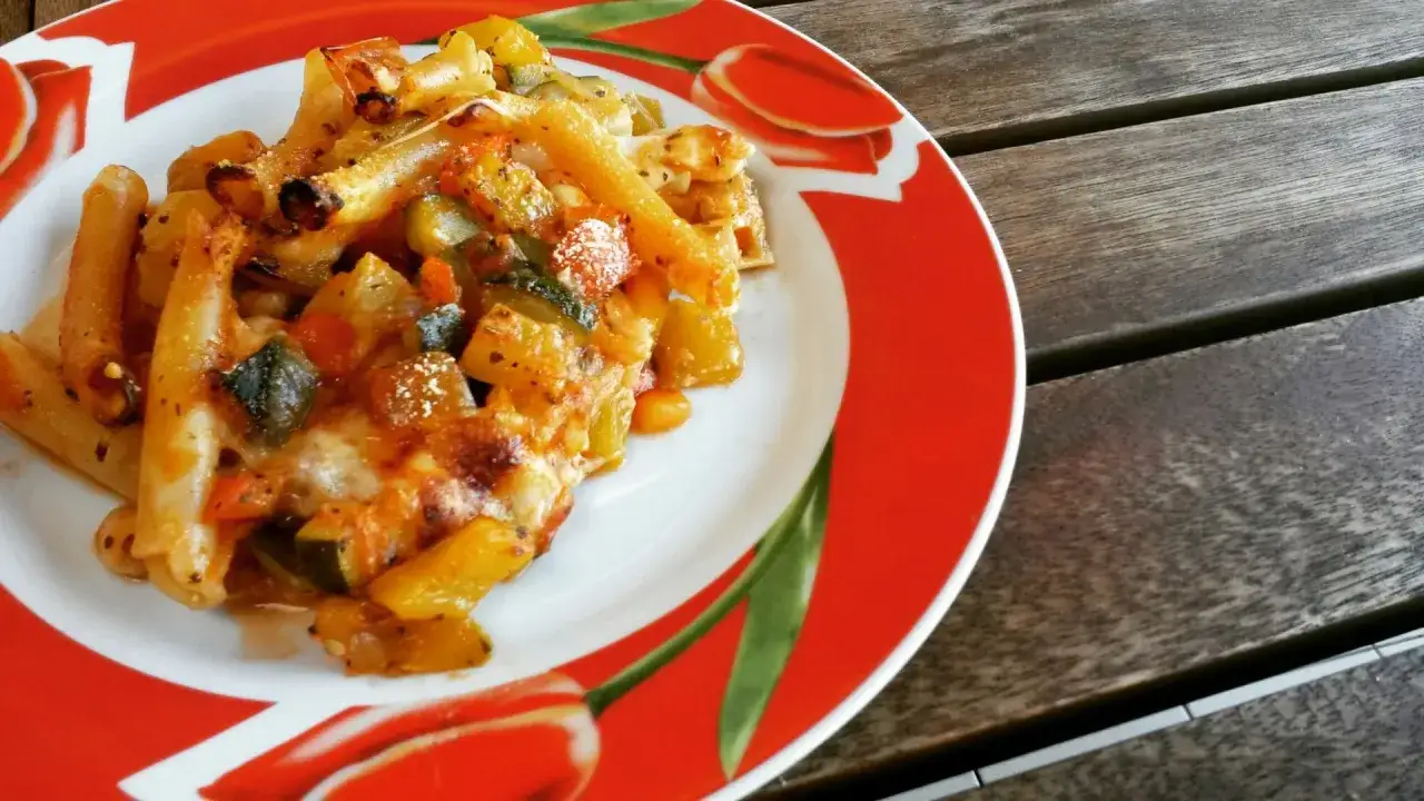 Piatto di pasta alla sorrentina con verdure e formaggio fuso, servito su un piatto rosso decorato.