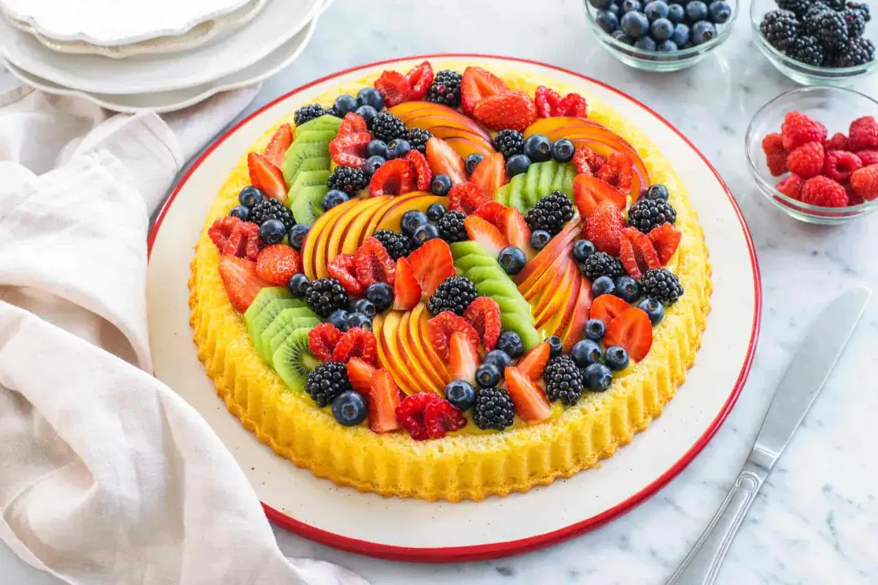 Crostata morbida alla frutta, un tripudio di colori con fragole, kiwi, pesche, mirtilli, lamponi e more che decorano una base soffice.