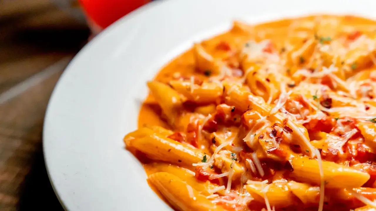 Piatto di penne al baffo cremose, condite con pomodoro e parmigiano grattugiato, pronte per essere gustate.