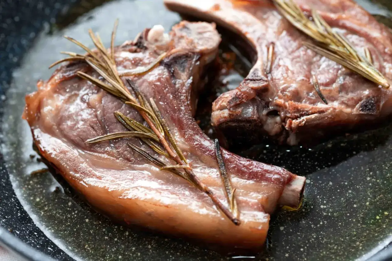 Due braciole di maiale succulente cuociono in padella con rametti di rosmarino, emanando un profumo invitante.