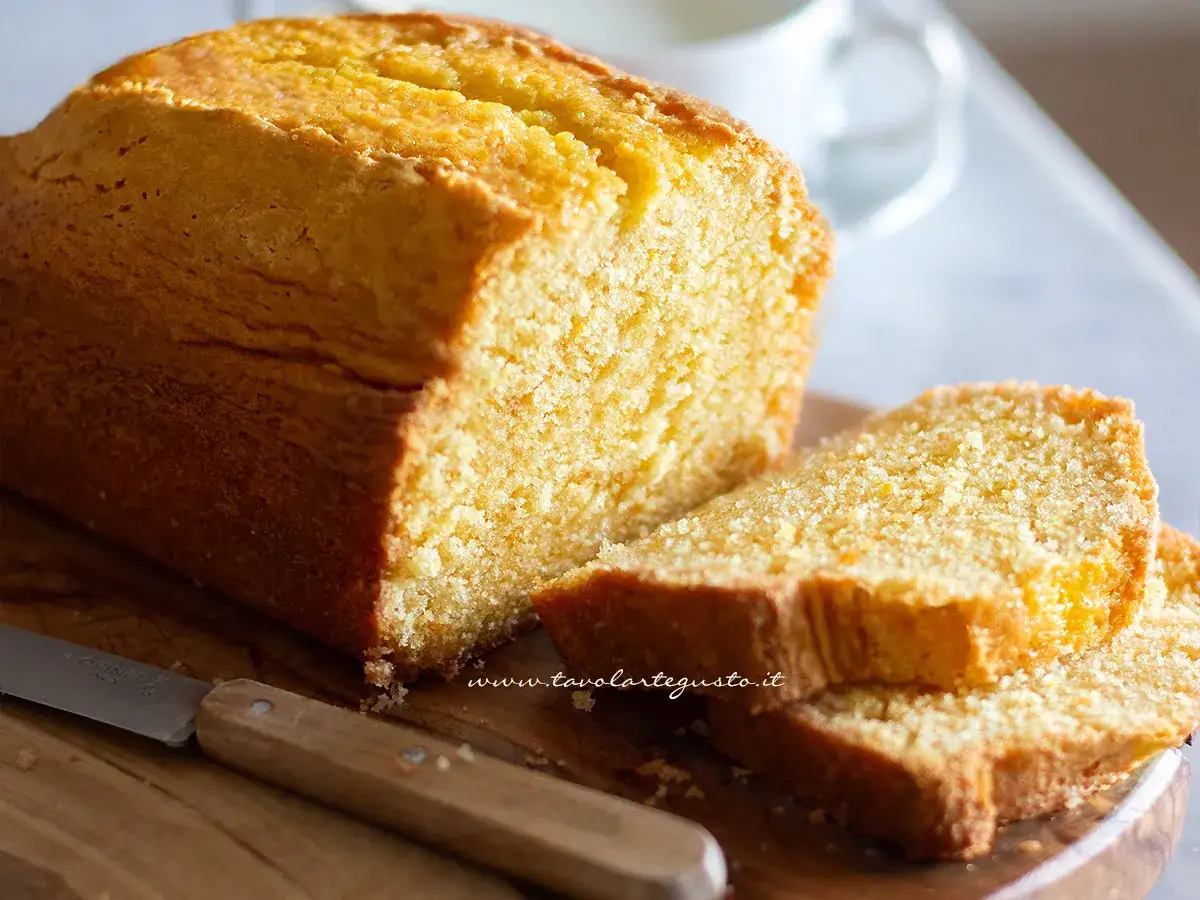 Plumcake senza uova dorato e soffice, tagliato a fette su un tagliere di legno con un coltello.