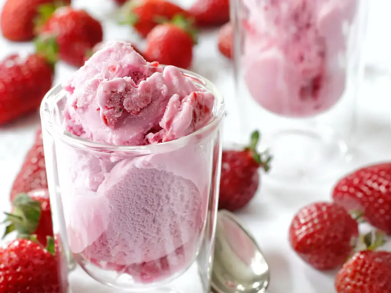 Un bicchiere colmo di cremoso gelato alla fragola, circondato da fragole fresche e succose.