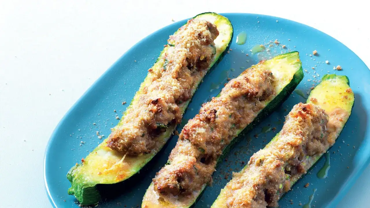 Tre zucchine tonde ripiene, gratinate al forno, servite su un piatto blu.
