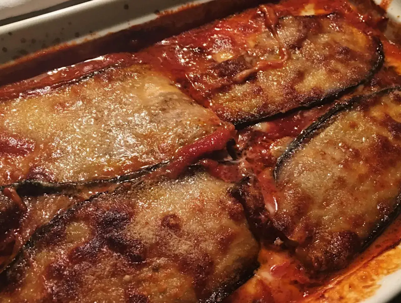 Parmigiana di melanzane appena sfornata, con strati dorati di melanzane, sugo rosso e formaggio filante.