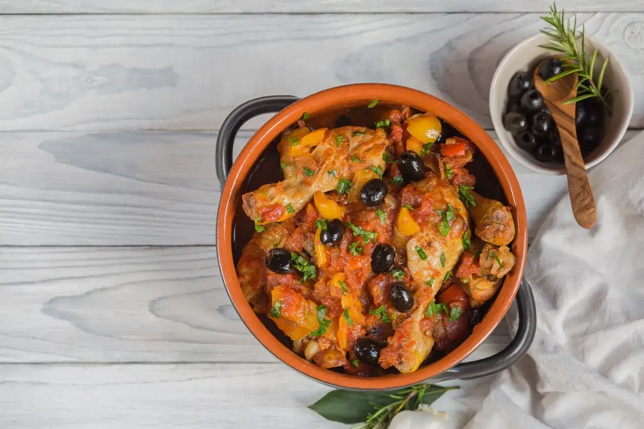 Un saporito pollo alla cacciatora in terracotta, con olive nere e peperoni, pronto per essere gustato.