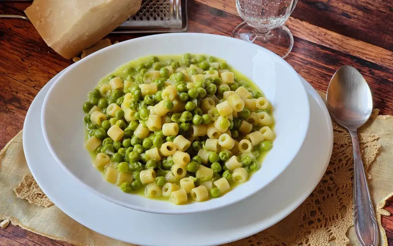Un piatto invitante di pasta e piselli, con un pezzo di parmigiano e una grattugia sullo sfondo.