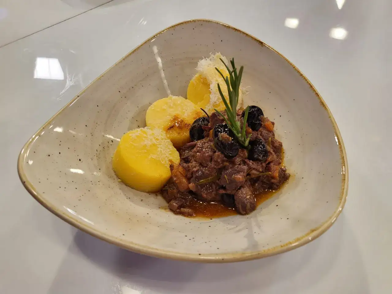 Cinghiale in umido fatto in casa da Benedetta, servito con polenta e olive nere, guarnito con rosmarino e parmigiano.
