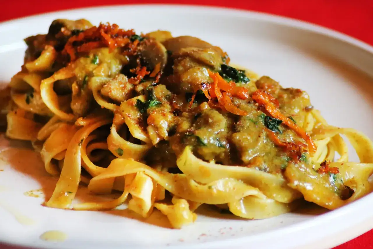 Tagliatelle ai funghi cremose, guarnite con scorza d'arancia e prezzemolo fresco. Un piatto invitante e saporito.