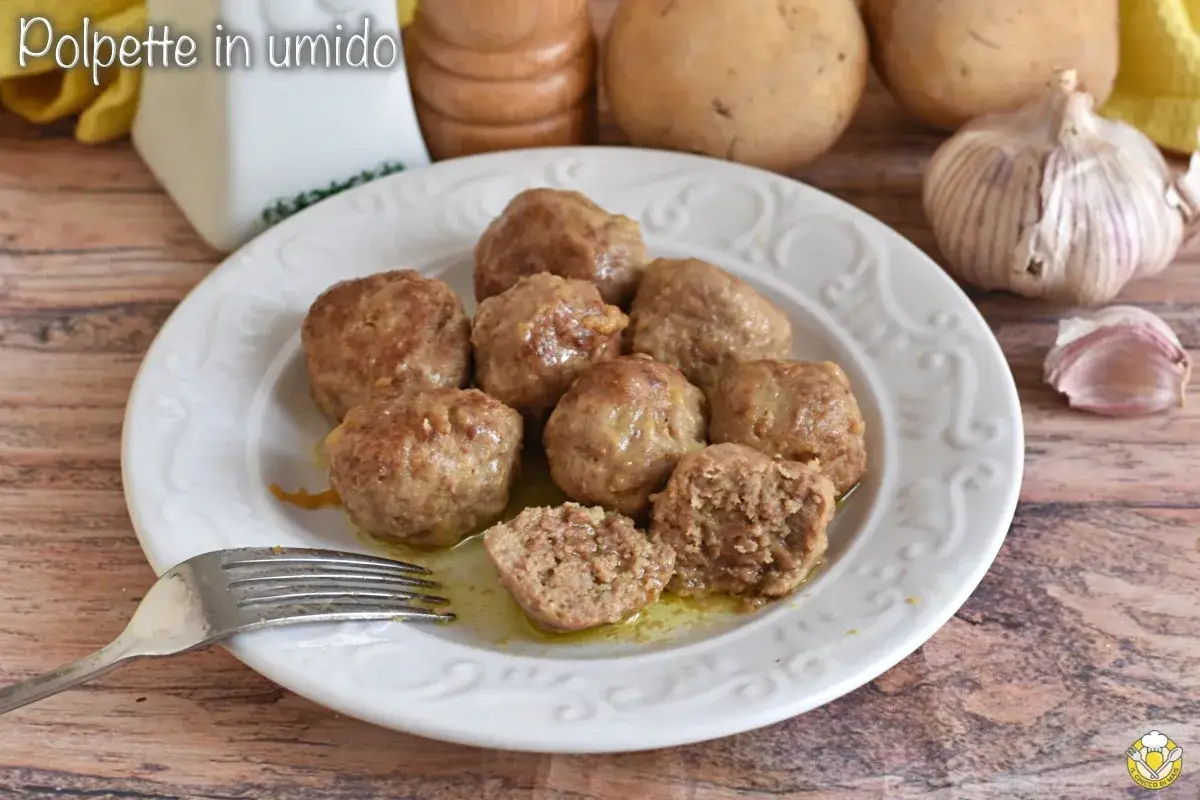 Piatto di polpette in bianco, morbide e succulente, pronte per essere gustate. Sullo sfondo, patate e aglio.