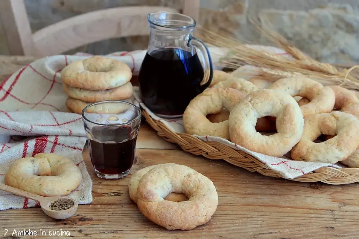 Ciambelline al vino dorate, fragranti e profumate, servite con un bicchiere di vino rosso e semi di finocchio.
