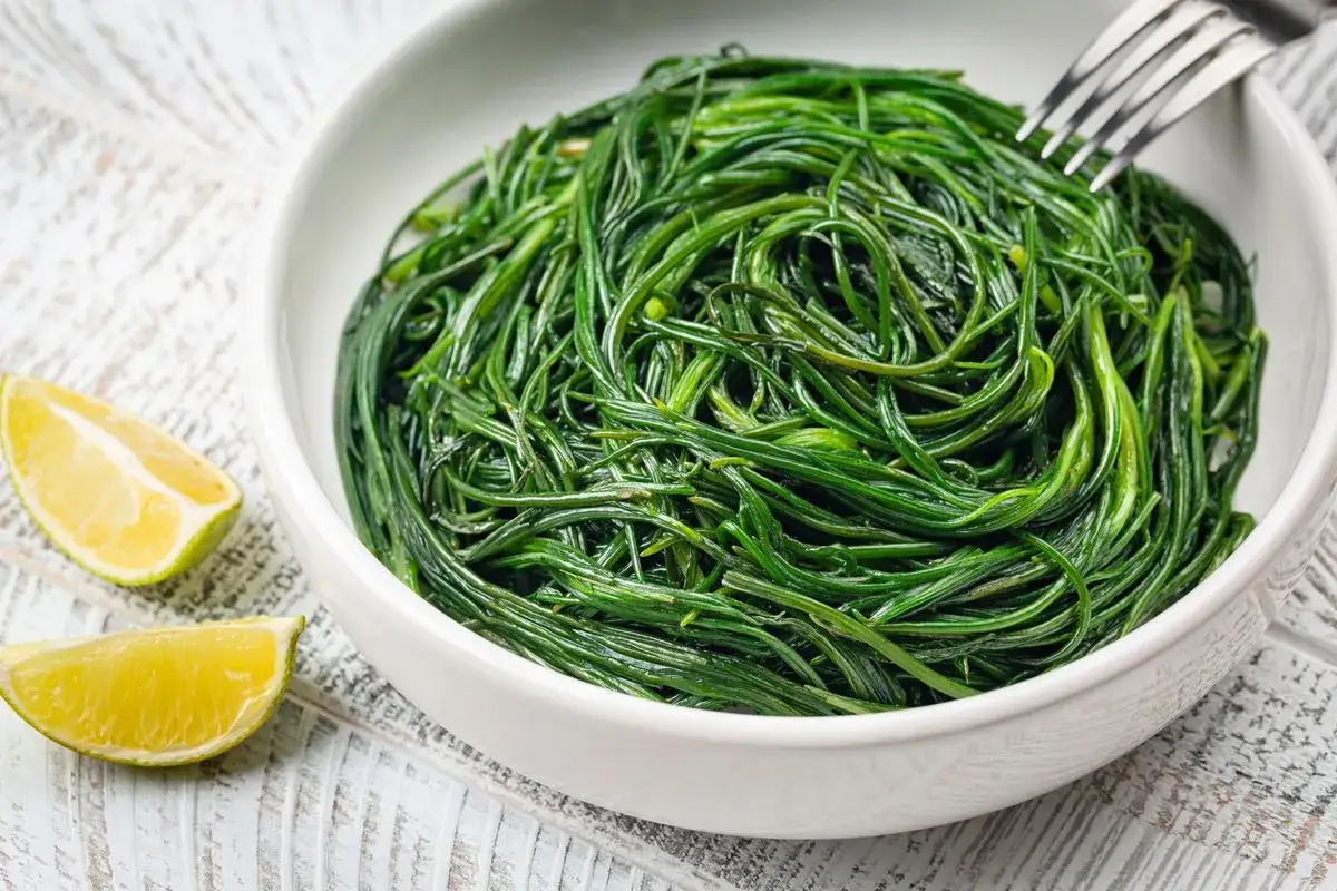 Agretti in padella, un contorno fresco e saporito, serviti in una ciotola bianca con spicchi di limone.