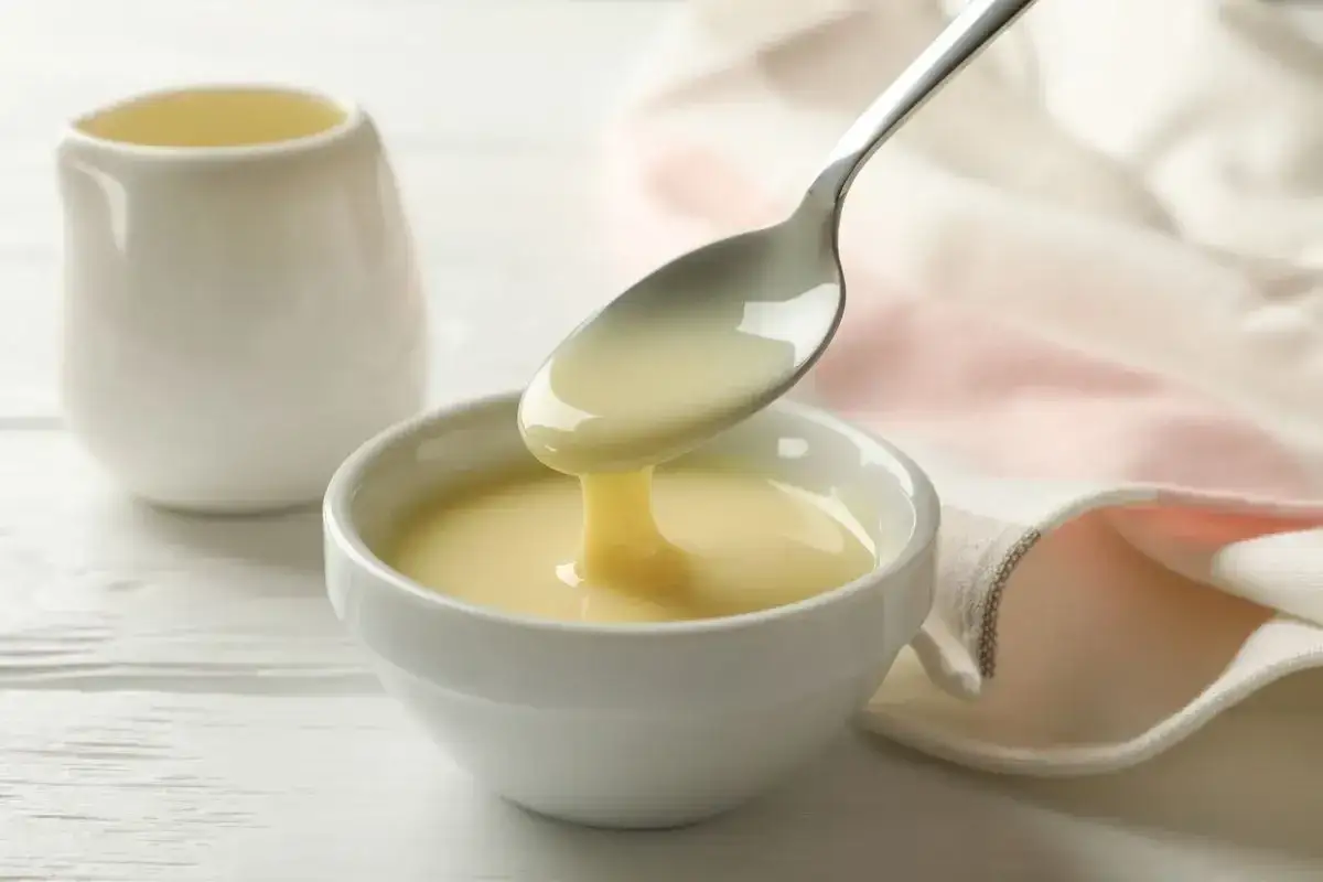 Latte condensato bimby versato da un cucchiaio in una ciotola bianca. Dolcezza cremosa pronta per dolci e caff&egrave;.