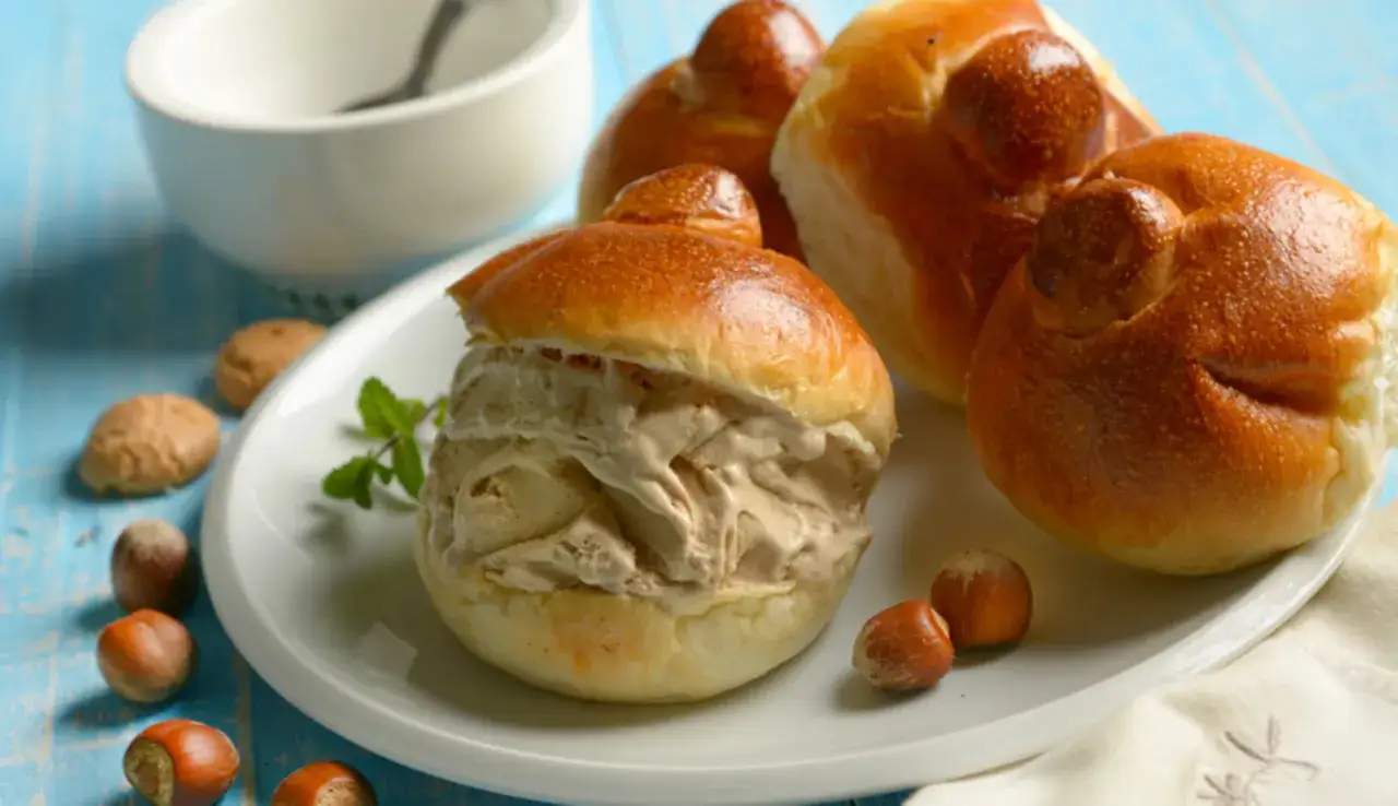 Brioche col tuppo farcito con gelato cremoso, su un piatto bianco con nocciole e menta.