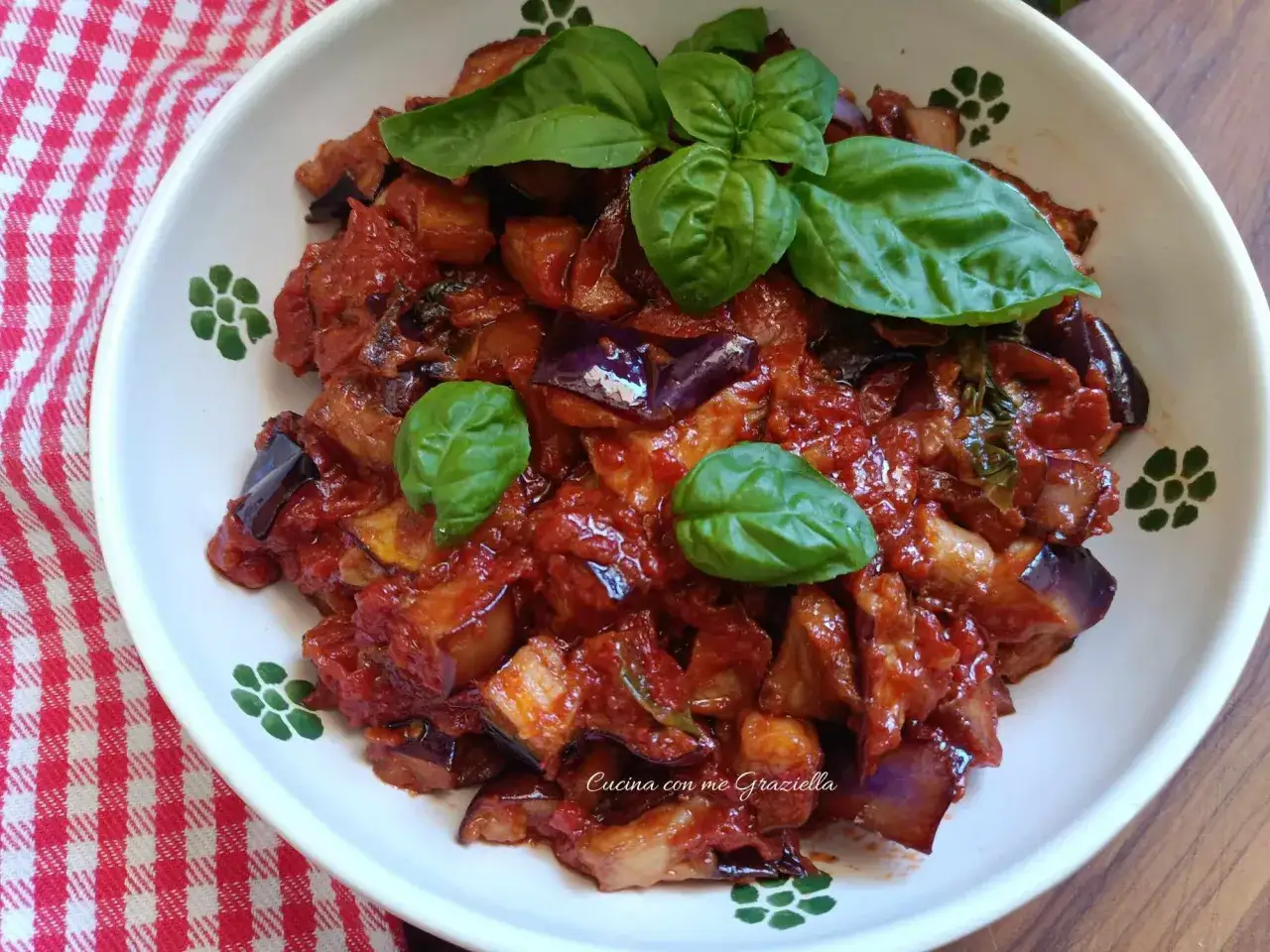 Melanzane a funghetto succulente, condite con pomodoro e basilico fresco, servite in un piatto bianco decorato.