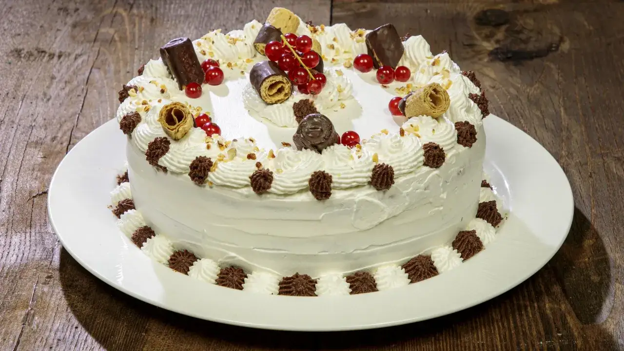 Torta decorata con panna, ribes, cioccolatini e un cuore di ganache al cioccolato.